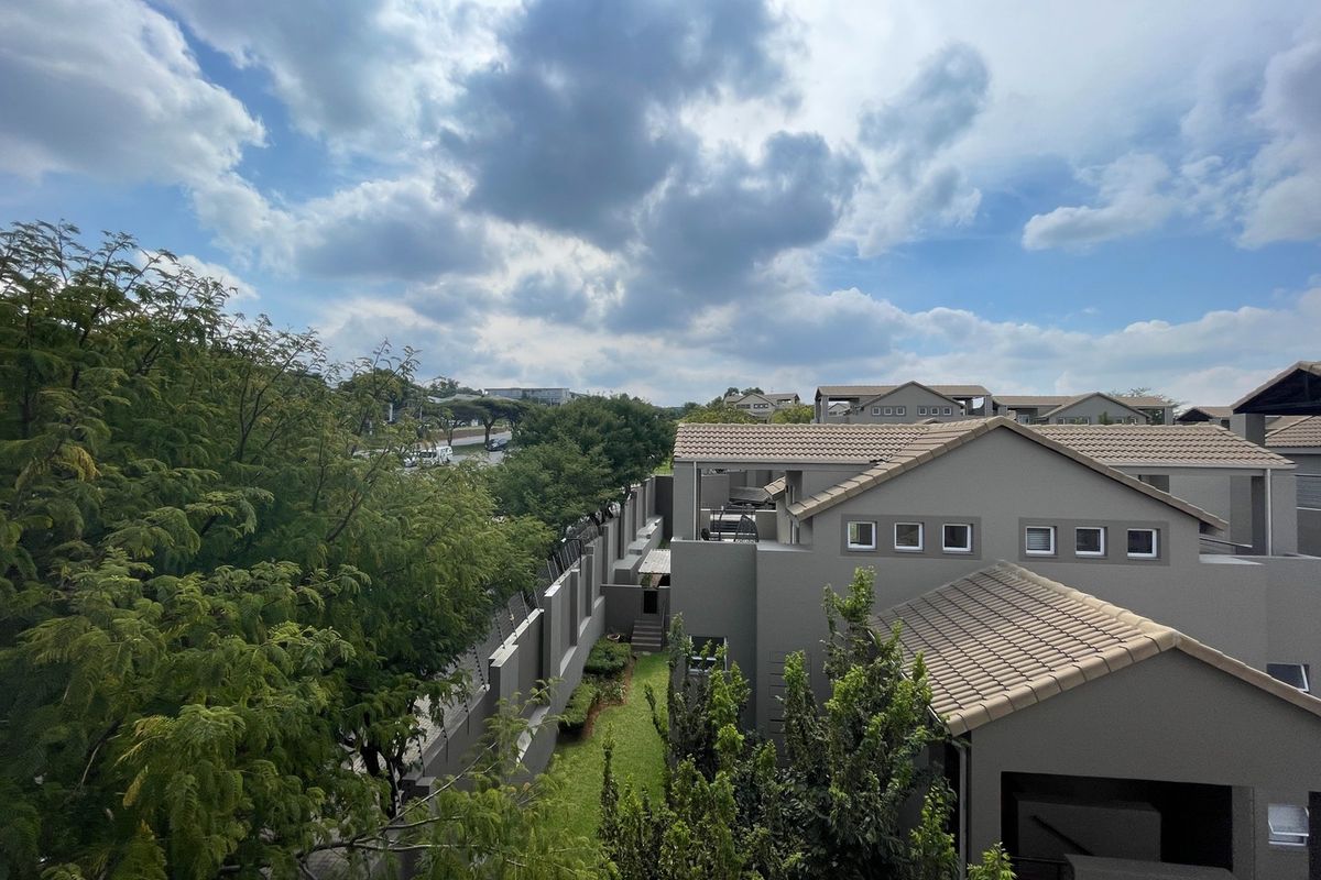 An elevated aerial view of the apartment complex, showcasing the tiled roof architecture, perimeter security fencing, and surrounding landscaped garden areas.