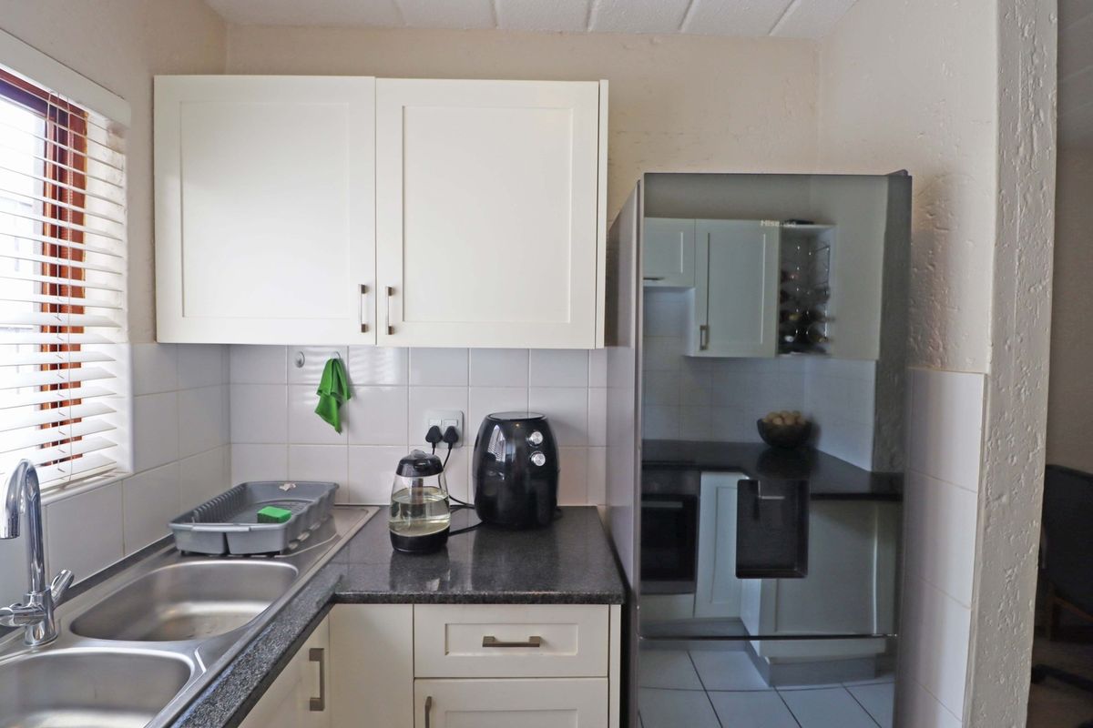 A functional kitchen featuring white cabinetry, dark laminate countertops, a double bowl stainless steel sink, and tiled splashbacks.