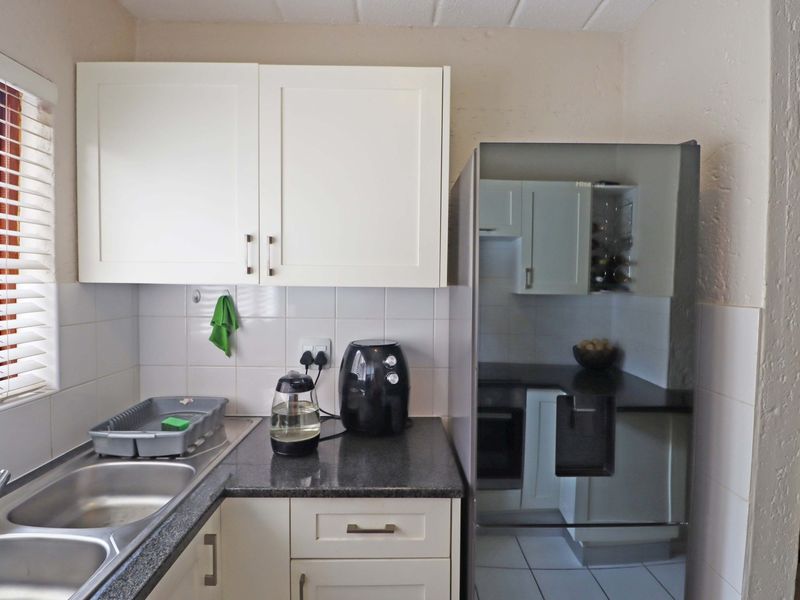 A functional kitchen featuring white cabinetry, dark laminate countertops, a double bowl stainless steel sink, and tiled splashbacks.