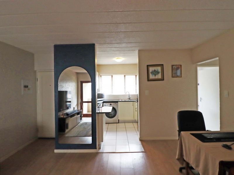 Open plan living area featuring a kitchen with built-in cabinetry and tiled flooring, transitioning into a laminate-floored living space with a decorative archway.