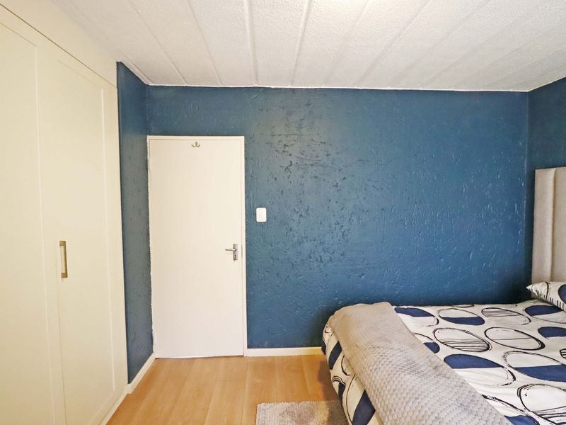A bedroom featuring laminate flooring, a built-in wardrobe, and a textured blue accent wall.