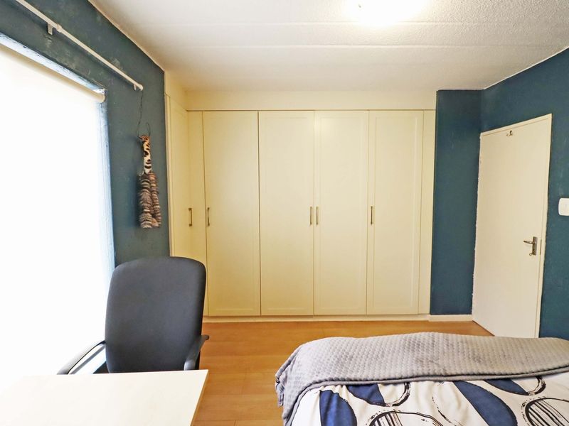 A bedroom featuring built-in cupboards, laminate flooring, and a large window with a curtain rail.
