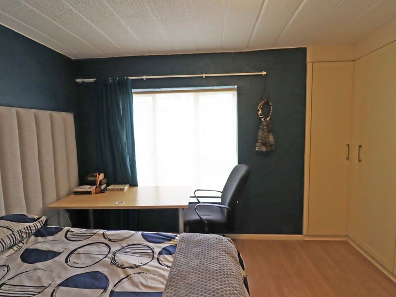 A bedroom featuring laminate flooring, a built-in wardrobe, and a textured ceiling, offering a functional space with dark accent walls.