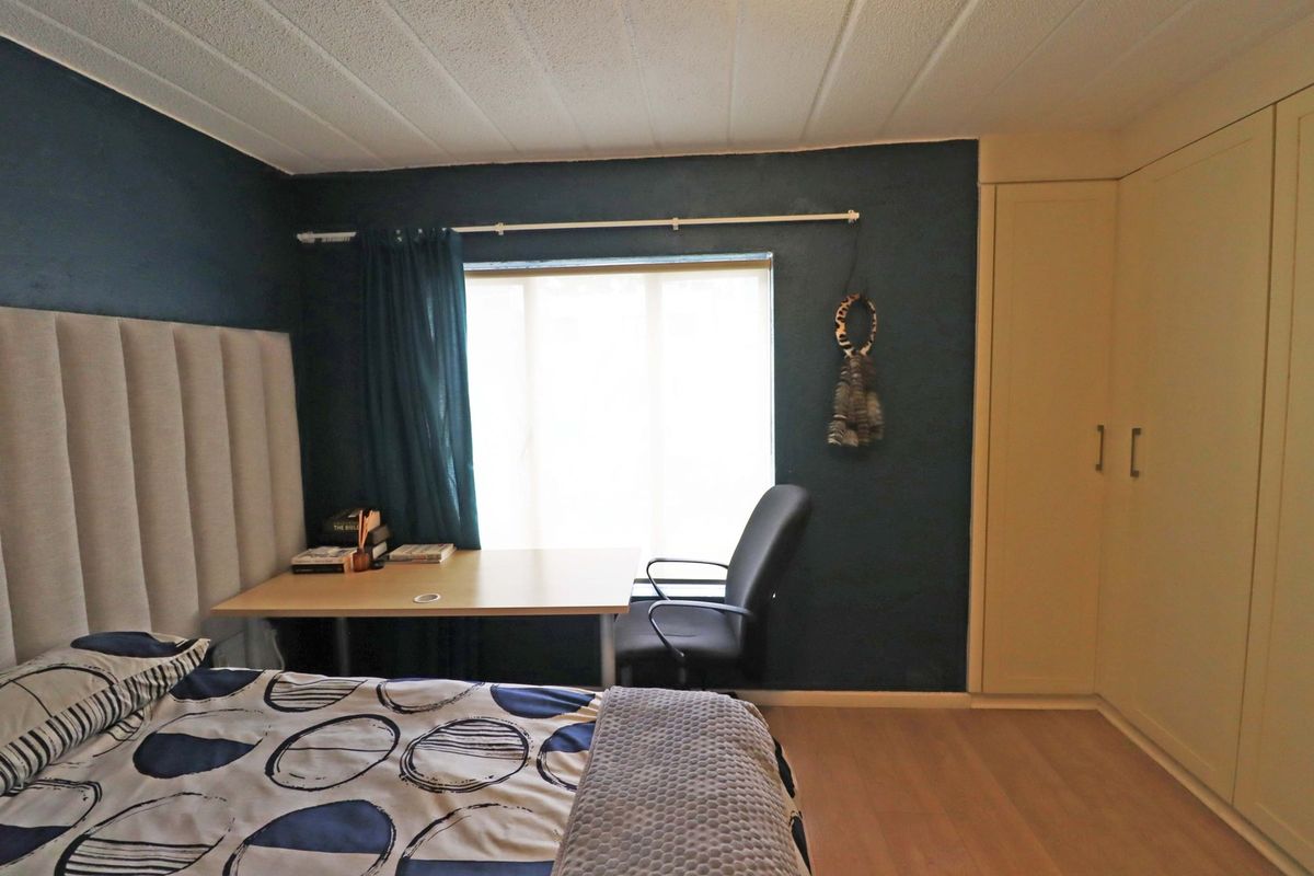 A bedroom featuring laminate flooring, a built-in wardrobe, and a textured ceiling, offering a functional space with dark accent walls.