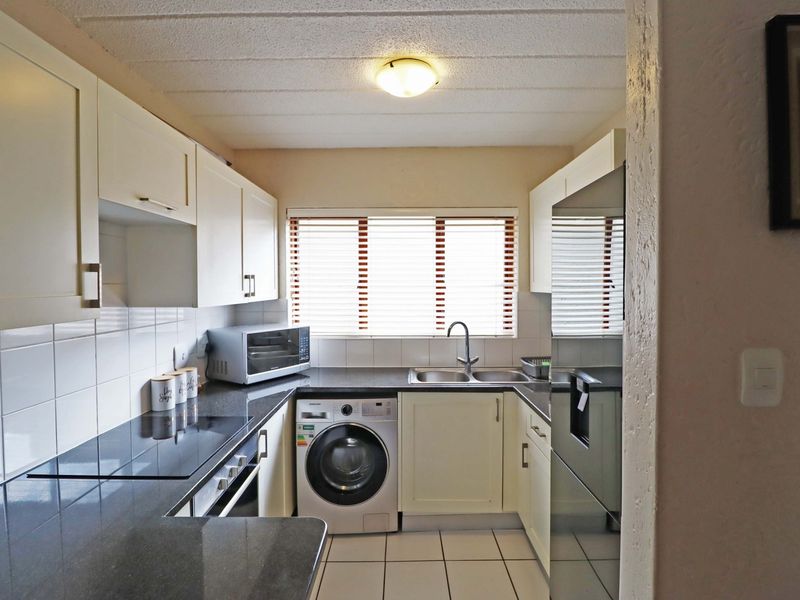 Compact kitchen featuring built-in cabinetry, stone countertops, tiled backsplash, integrated appliances, and ceramic tile flooring with a functional layout.