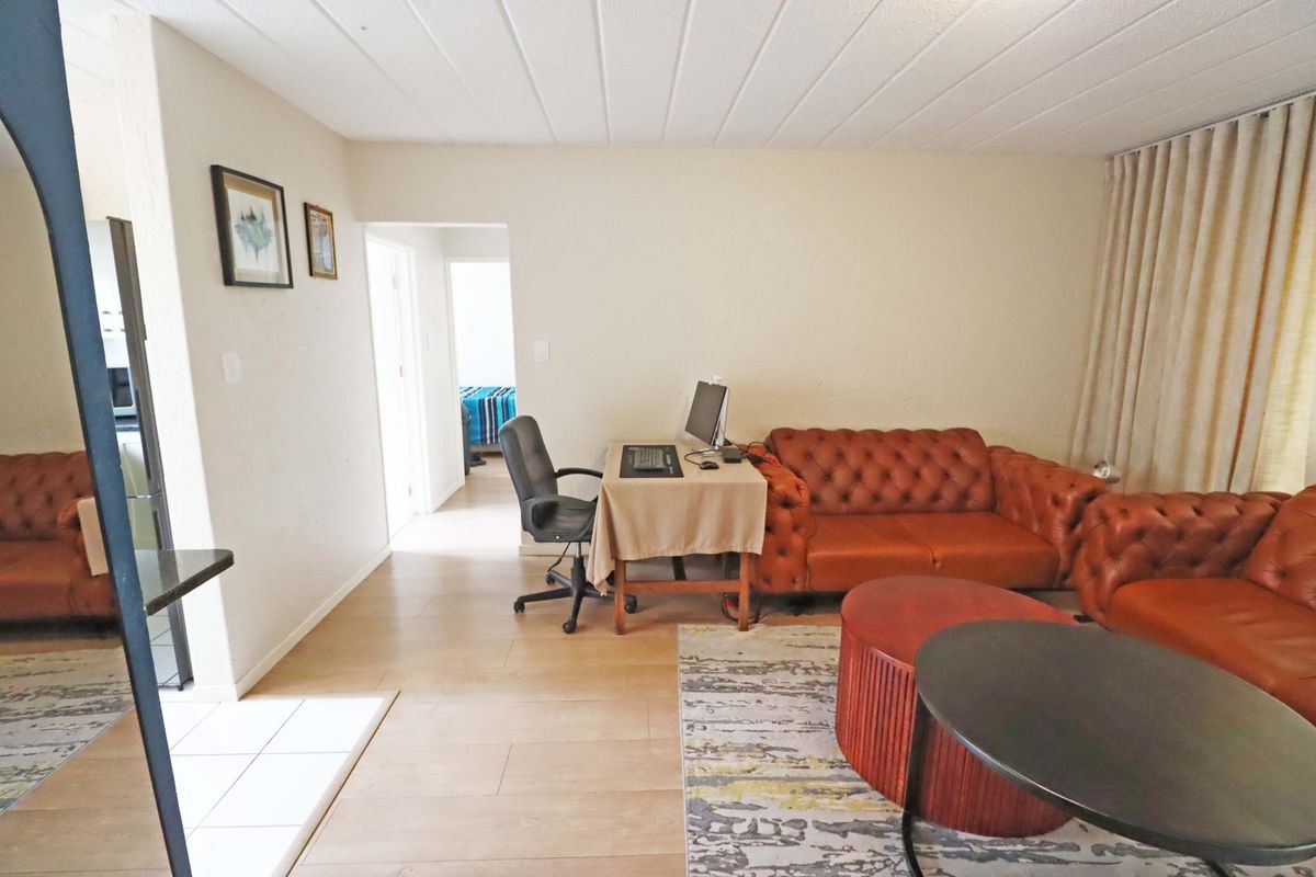 A living room area featuring tiled flooring and a textured ceiling, with an open layout leading to an adjacent bedroom.