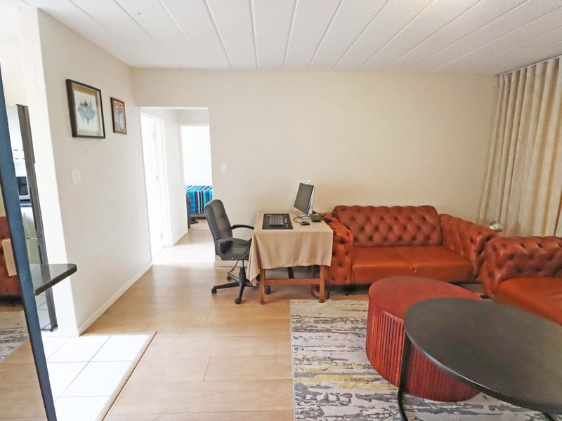 A living room area featuring tiled flooring and a textured ceiling, with an open layout leading to an adjacent bedroom.