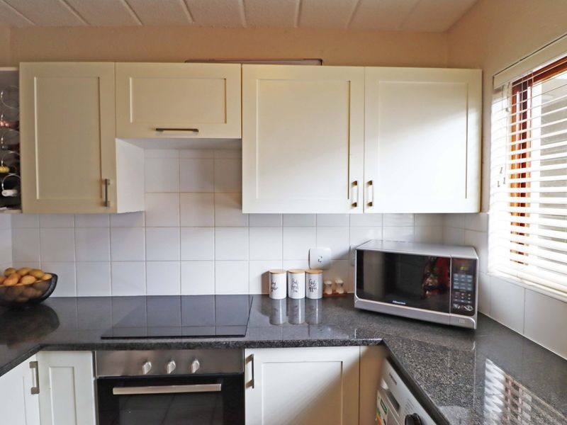 A well-maintained kitchen featuring cream cabinetry, dark granite countertops, a tiled backsplash, and integrated cooking appliances.