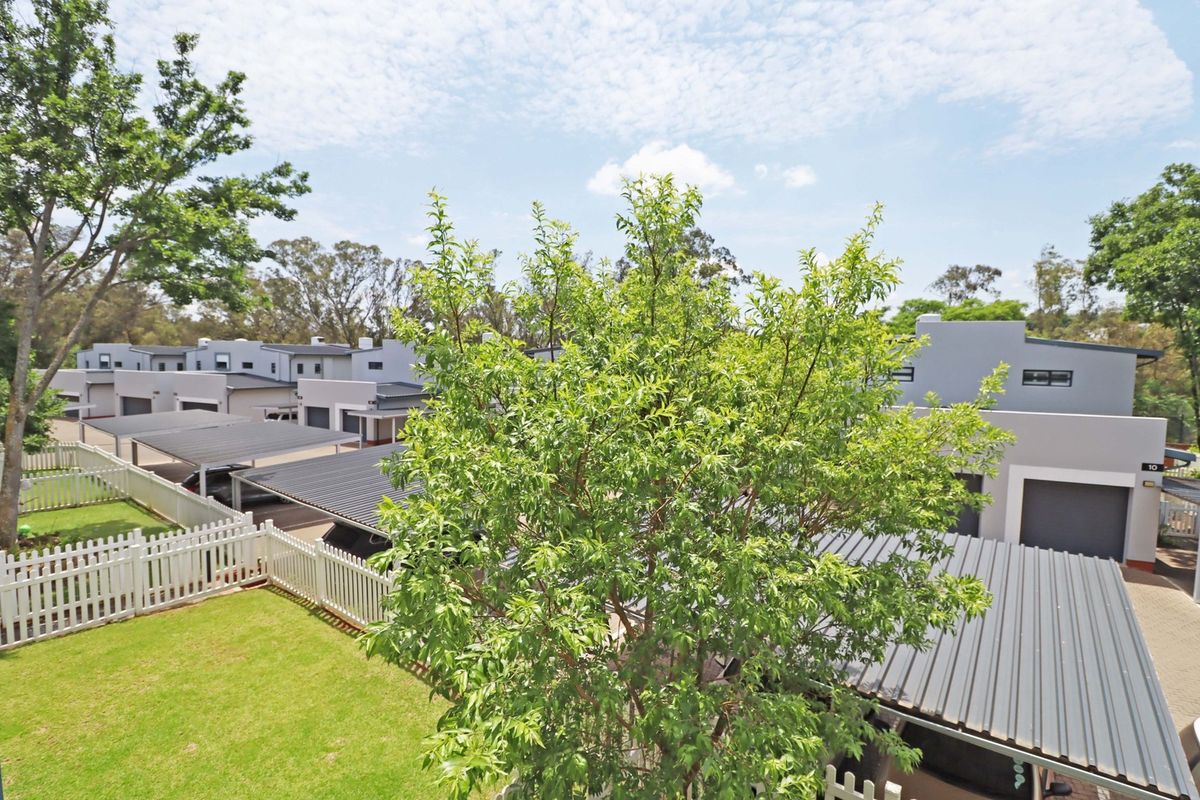 An elevated view of the apartment complex grounds, featuring covered parking bays, a well-maintained lawn, and white picket fencing.