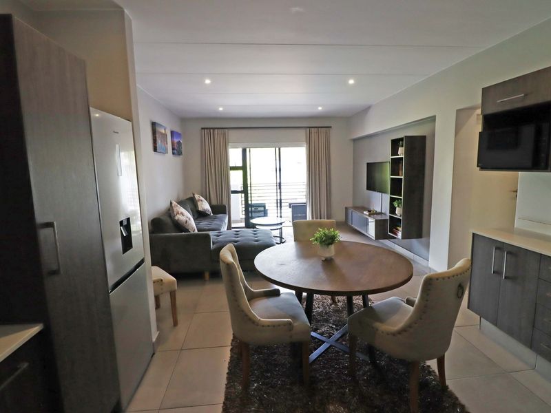 An open-plan living and dining area featuring tiled floors, recessed lighting, and modern cabinetry, with direct access to a balcony through sliding glass doors.