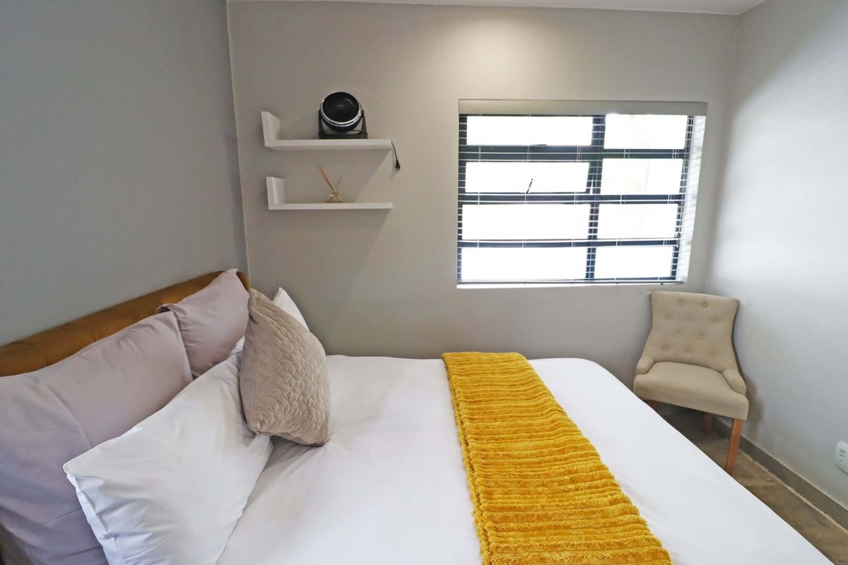 A well-maintained bedroom featuring neutral wall tones, built-in floating shelving, and a horizontal slat window providing natural light.