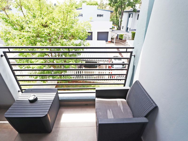 A private balcony featuring tiled flooring and a secure metal balustrade, overlooking the complex grounds and parking area.
