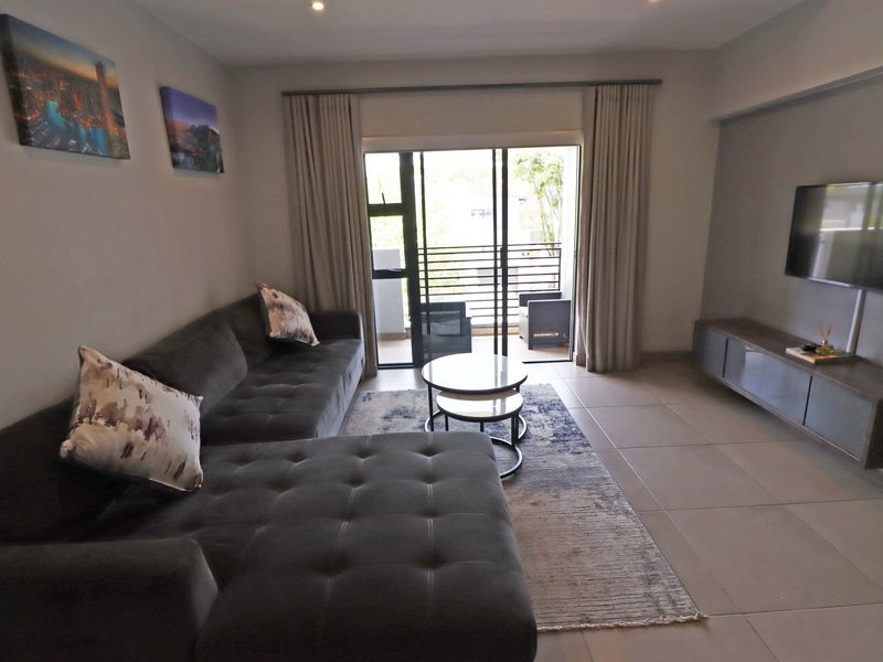 A well-maintained living room featuring neutral tiled flooring, recessed lighting, and direct access to a private balcony through sliding glass doors.