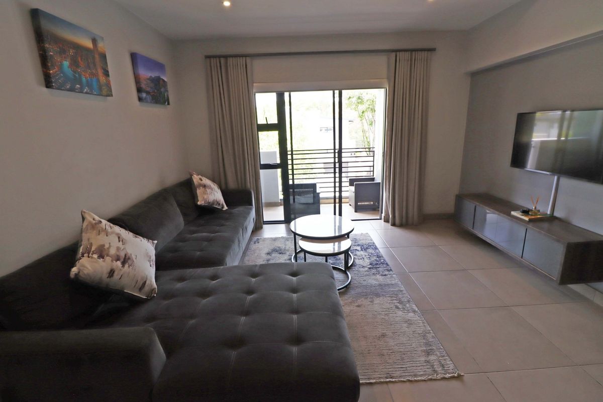 A well-maintained living room featuring neutral tiled flooring, recessed lighting, and direct access to a private balcony through sliding glass doors.