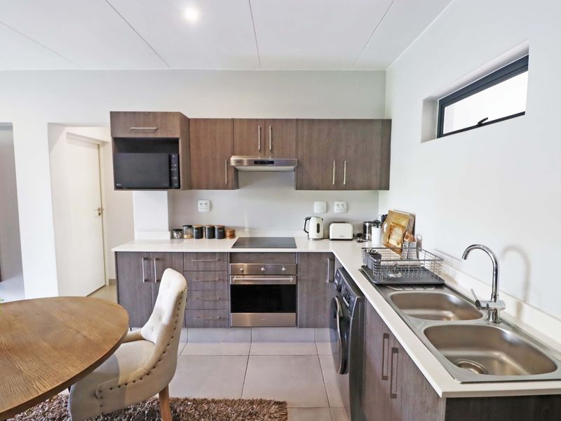 Modern kitchen featuring dark wood cabinetry, white countertops, integrated appliances, and a double stainless steel sink, offering a clean and functional cooking space.