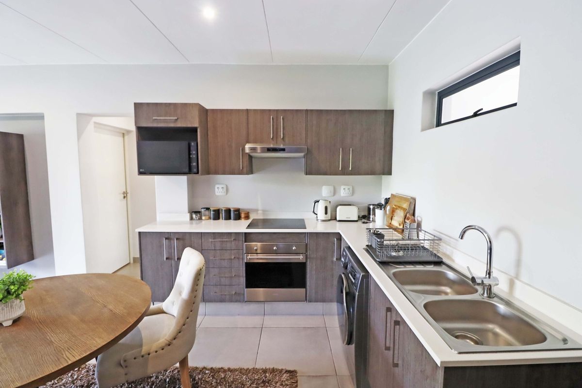 Modern kitchen featuring dark wood cabinetry, white countertops, integrated appliances, and a double stainless steel sink, offering a clean and functional cooking space.