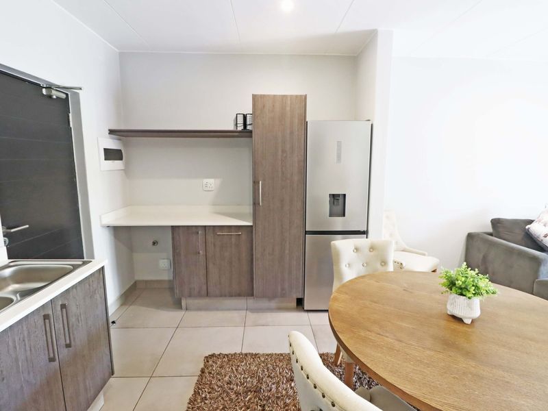 An open-plan living and kitchen area featuring modern wood-finish cabinetry, tiled flooring, and a functional layout suitable for contemporary apartment living.