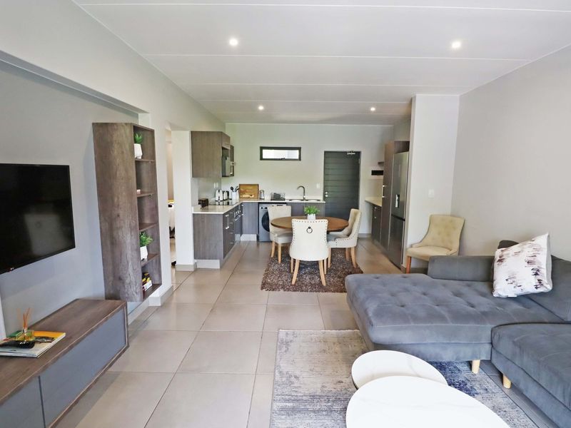 Modern open-plan living area featuring a contemporary kitchen with built-in cabinetry, tiled flooring, and recessed lighting, seamlessly flowing into the dining and lounge space.