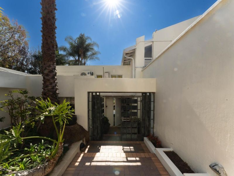 A bright front entrance featuring a paved walkway, secure metal gate, and established garden beds leading to the main building facade.