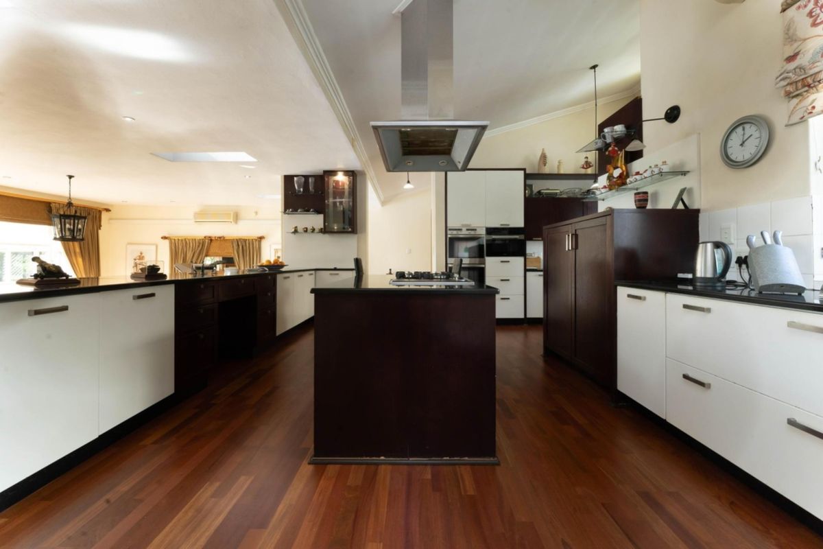 Spacious kitchen featuring a central island, built-in oven, extractor fan, gas hob, and modern cabinetry with rich hardwood flooring.