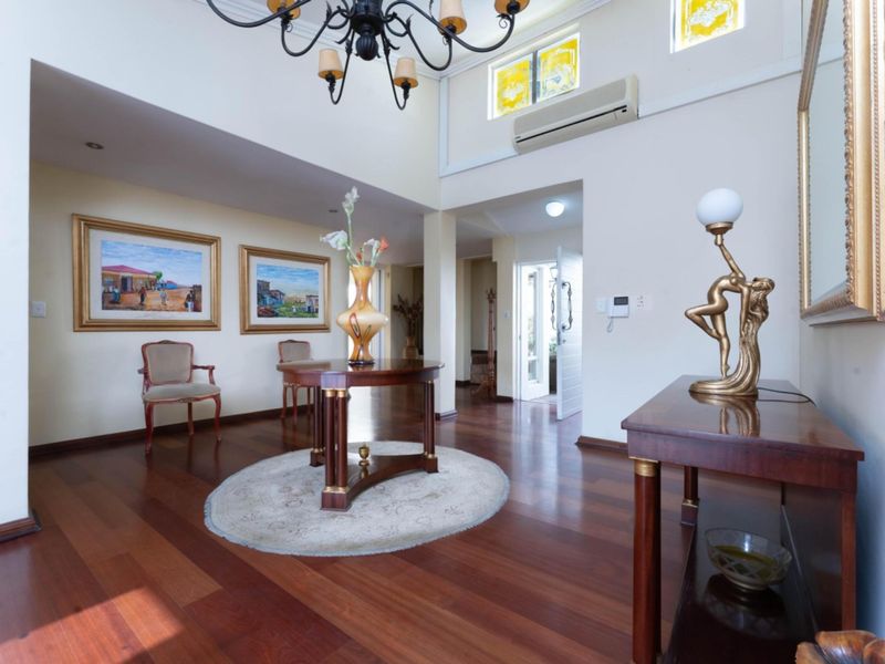 Spacious entrance hall featuring polished hardwood flooring, high ceilings with a decorative chandelier, and a wall-mounted air conditioning unit.