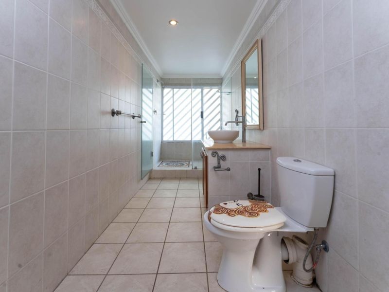 A functional bathroom featuring tiled walls and floors, a vanity with a vessel sink, and a glass-enclosed shower area.