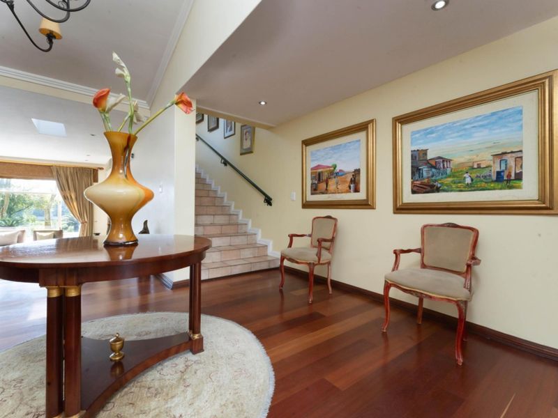 Spacious entrance hall featuring rich hardwood flooring, a tiled staircase with a handrail, and recessed lighting, leading into an open-plan living area.