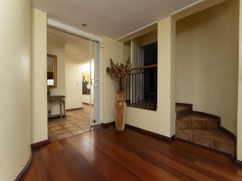 A spacious hallway featuring warm hardwood flooring, a tiled staircase with a wrought iron balustrade, and access to adjacent living areas.
