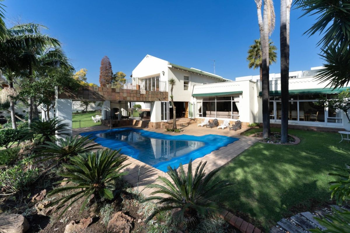Rear view of the property featuring a swimming pool, tiled patio area, covered pergola, and a well-maintained garden with mature palm trees.