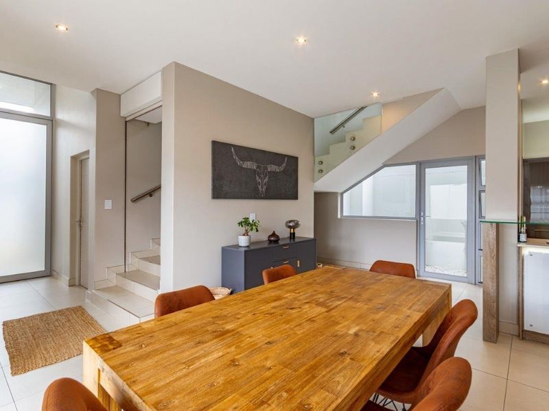 Modern open-plan living area featuring tiled floors, recessed lighting, and a contemporary staircase with a glass balustrade, seamlessly connecting to the kitchen space.