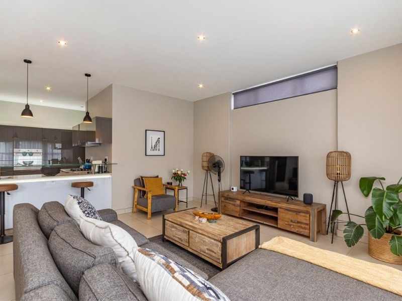 A modern open-plan living area featuring a kitchen with a breakfast island, neutral wall tones, recessed lighting, and tiled flooring throughout.