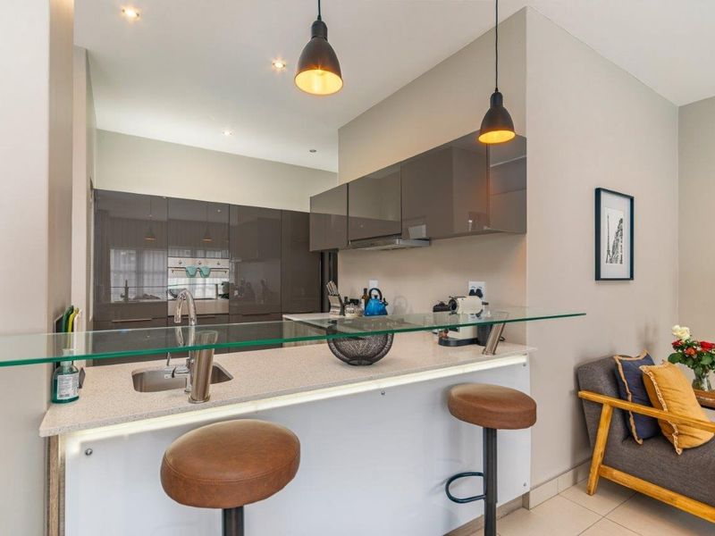 Modern kitchen featuring sleek glossy cabinetry, stone countertops, a glass breakfast bar, and integrated appliances with stylish pendant lighting.