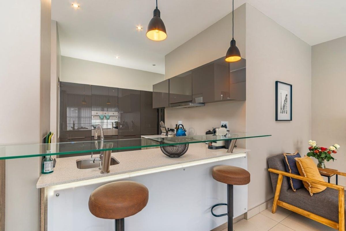 Modern kitchen featuring sleek glossy cabinetry, stone countertops, a glass breakfast bar, and integrated appliances with stylish pendant lighting.