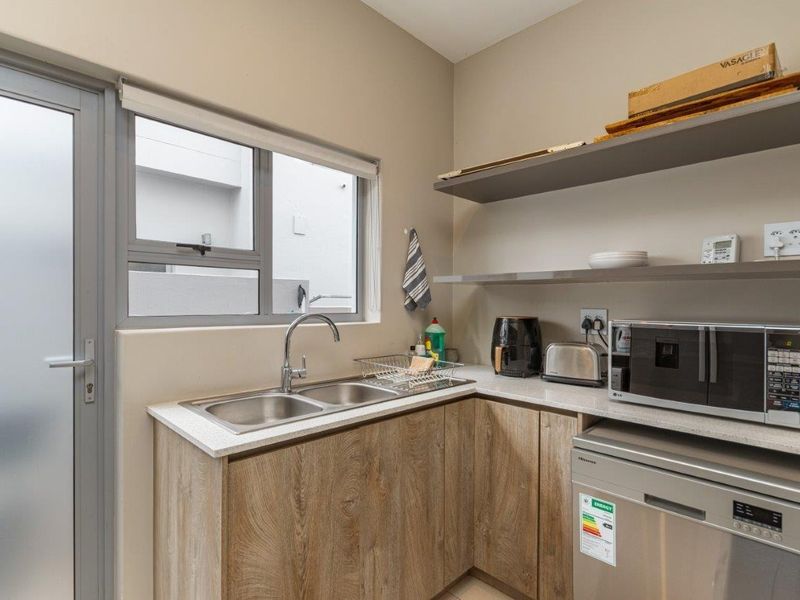 A functional scullery featuring wood-look cabinetry, stone countertops, a double bowl sink, and open shelving, providing convenient additional prep and wash-up space.