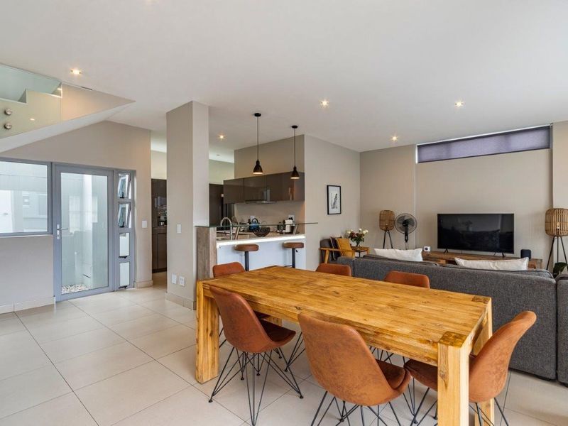 Modern open-plan living area featuring a contemporary kitchen with island, dining space, and a staircase with glass balustrade, finished with neutral tiled flooring.