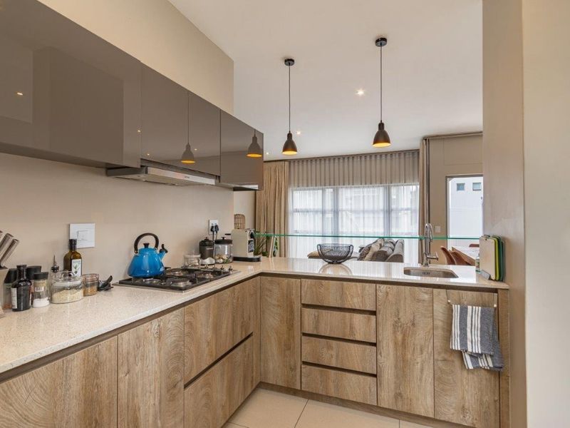 Modern open-plan kitchen featuring wood-grain cabinetry, stone countertops, gas hob, and integrated extractor fan, flowing seamlessly into the adjacent living area.