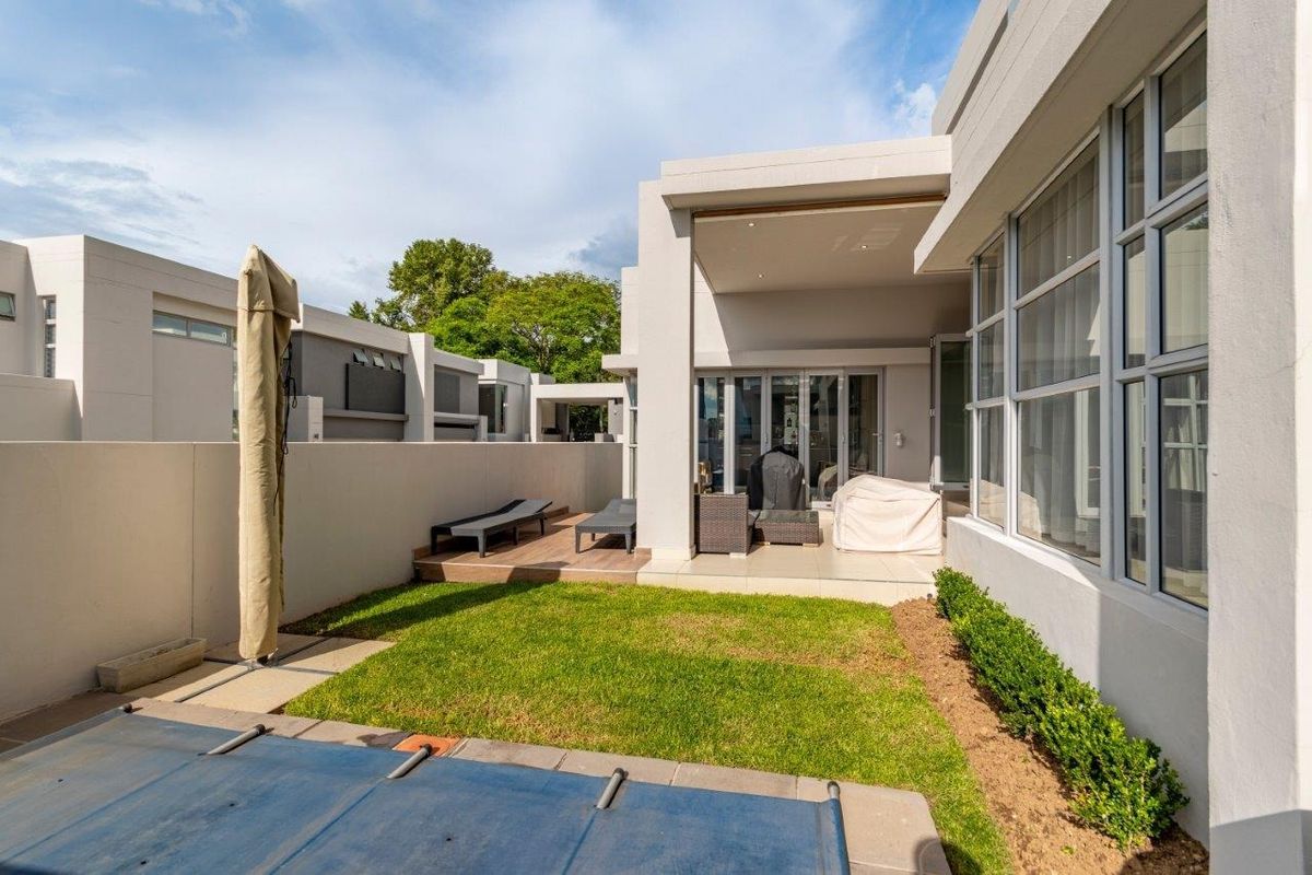 A well-maintained rear exterior featuring a covered patio, timber decking, a small lawn, and a swimming pool with a cover.
