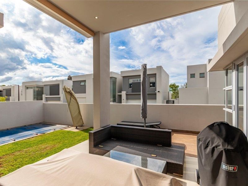 A covered patio area featuring tiled flooring and recessed lighting, overlooking a private garden with a swimming pool.