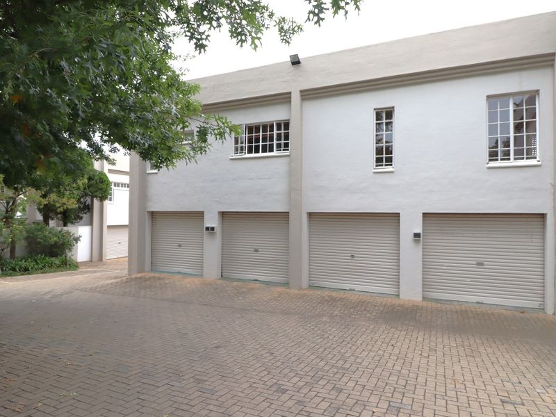 Exterior view of an apartment complex featuring four individual roller garage doors and a paved driveway area.