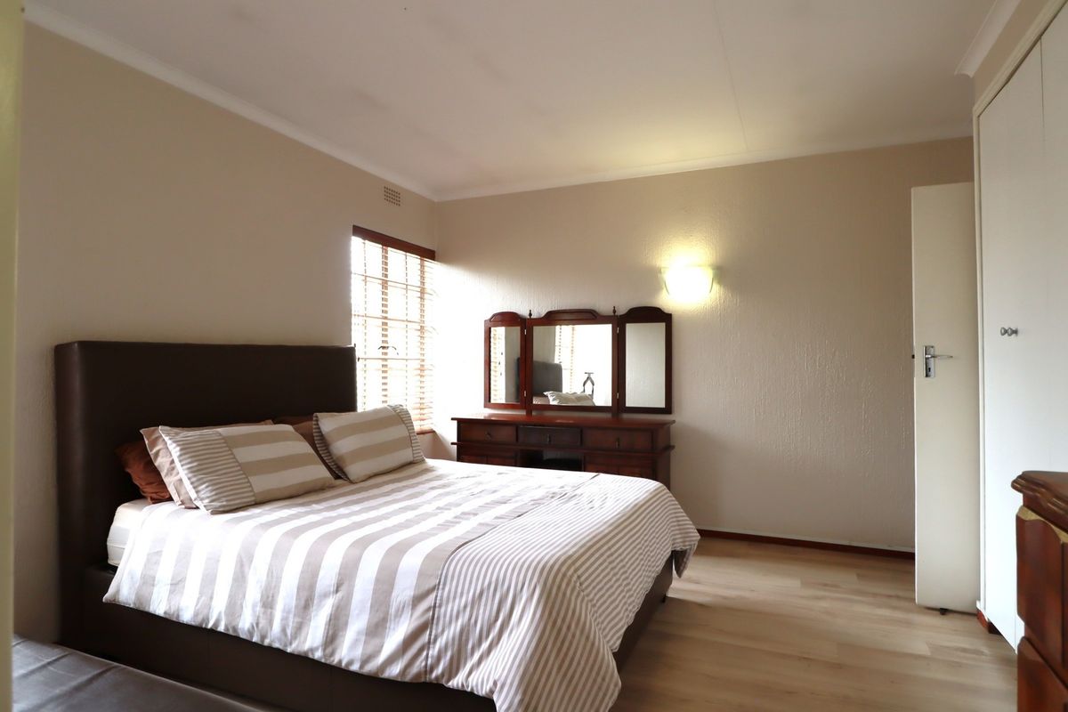 A well-lit bedroom featuring laminate flooring, a built-in wardrobe, and neutral wall finishes, providing a comfortable and functional living space.