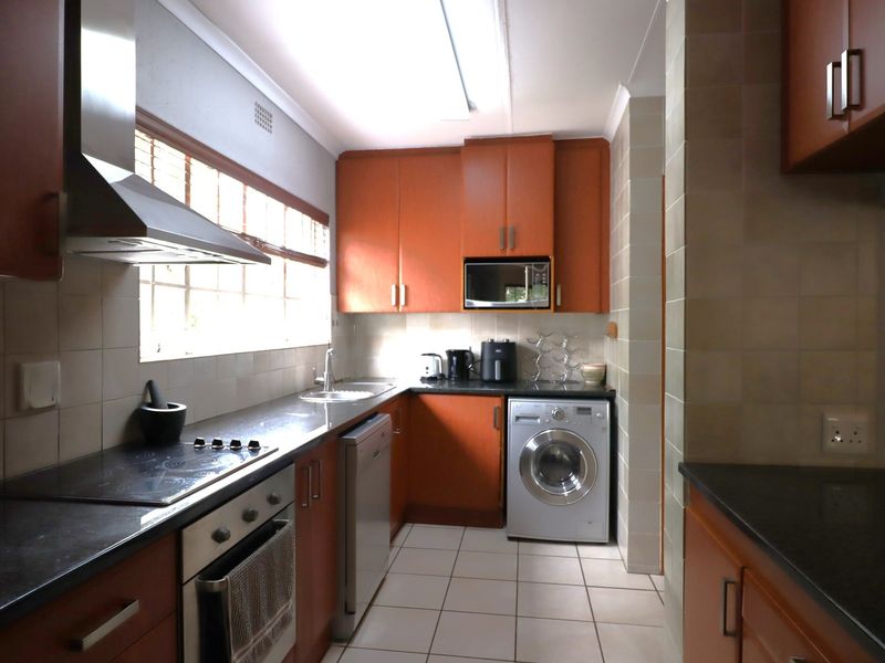 A functional kitchen featuring wood-tone cabinetry, dark countertops, integrated appliances, and tiled finishes, offering a practical layout for daily meal preparation.