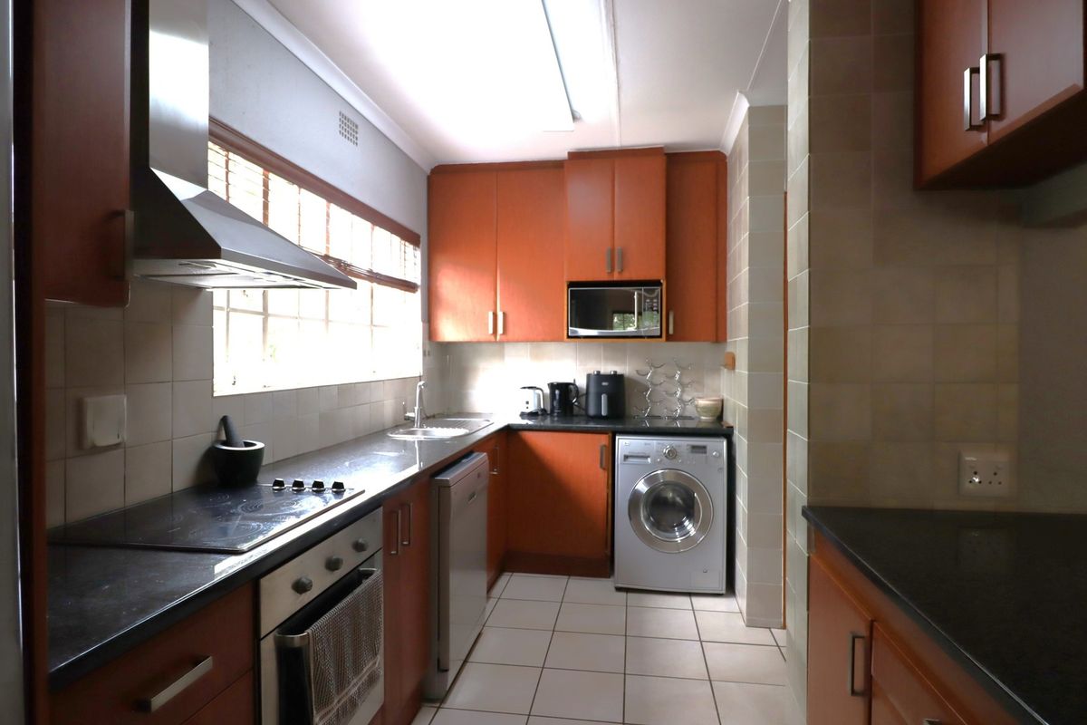 A functional kitchen featuring wood-tone cabinetry, dark countertops, integrated appliances, and tiled finishes, offering a practical layout for daily meal preparation.