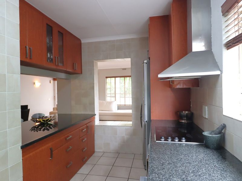 A functional kitchen featuring wooden cabinetry, granite countertops, an electric hob with extractor fan, and tiled finishes throughout.