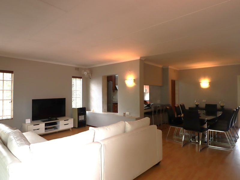 An open-plan living and dining area featuring laminate flooring, wall-mounted lighting, and a breakfast counter connecting to the kitchen space.