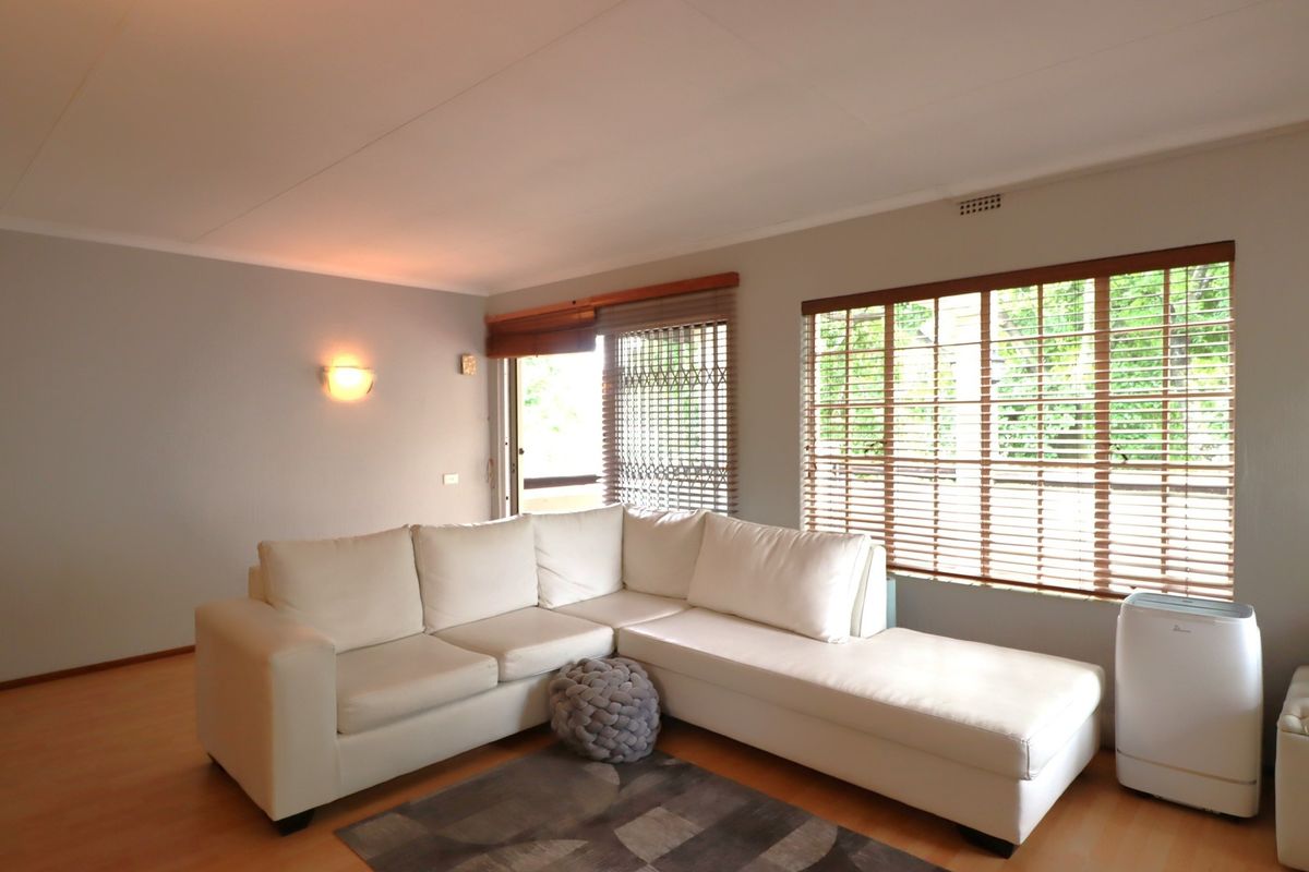 A bright living room featuring laminate flooring, wooden venetian blinds, and a security gate leading to an outdoor area.