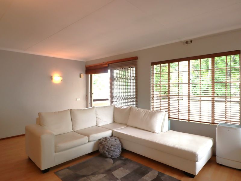 A bright living room featuring laminate flooring, wooden venetian blinds, and a security gate leading to an outdoor area.