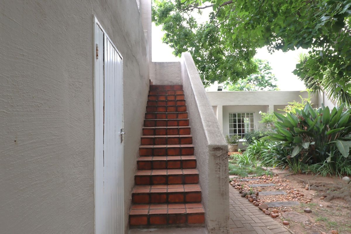 An exterior view of a tiled staircase leading to an upper level, adjacent to a paved garden path and building facade.