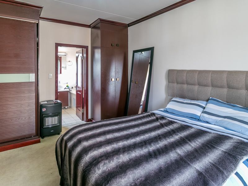 A bedroom featuring built-in dark wood cupboards, crown molding, and direct access to an en-suite bathroom.