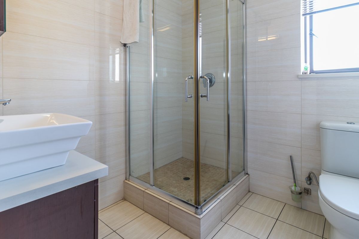 A clean, functional bathroom featuring a glass-enclosed shower, a modern vessel sink on a vanity cabinet, and neutral wall and floor tiling.