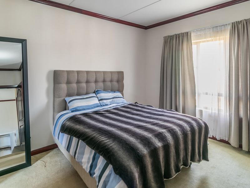 A well-lit bedroom featuring neutral walls, crown molding, and large windows with curtains, providing a comfortable and functional living space.
